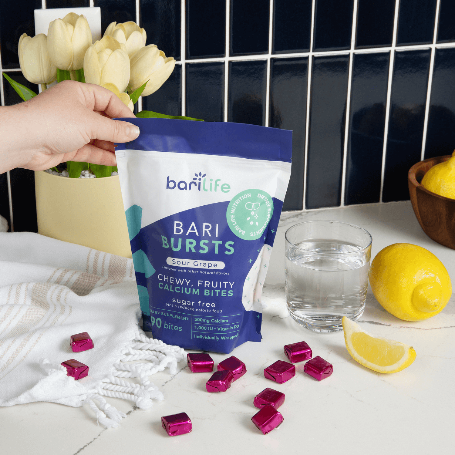 BariBurst calcium chews in sour grape flavor, displayed with fresh lemons and a glass of water on a kitchen counter.